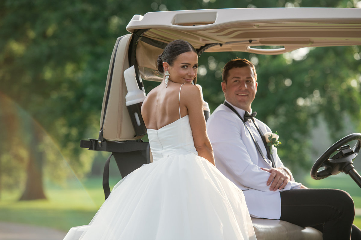 groom sitting in golf cart with bride standing smiling at The Muttontown Club