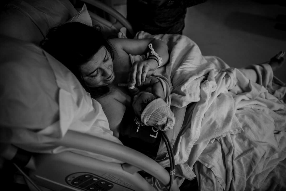 Black and white photo of a woman lying on a bed holding a newborn baby