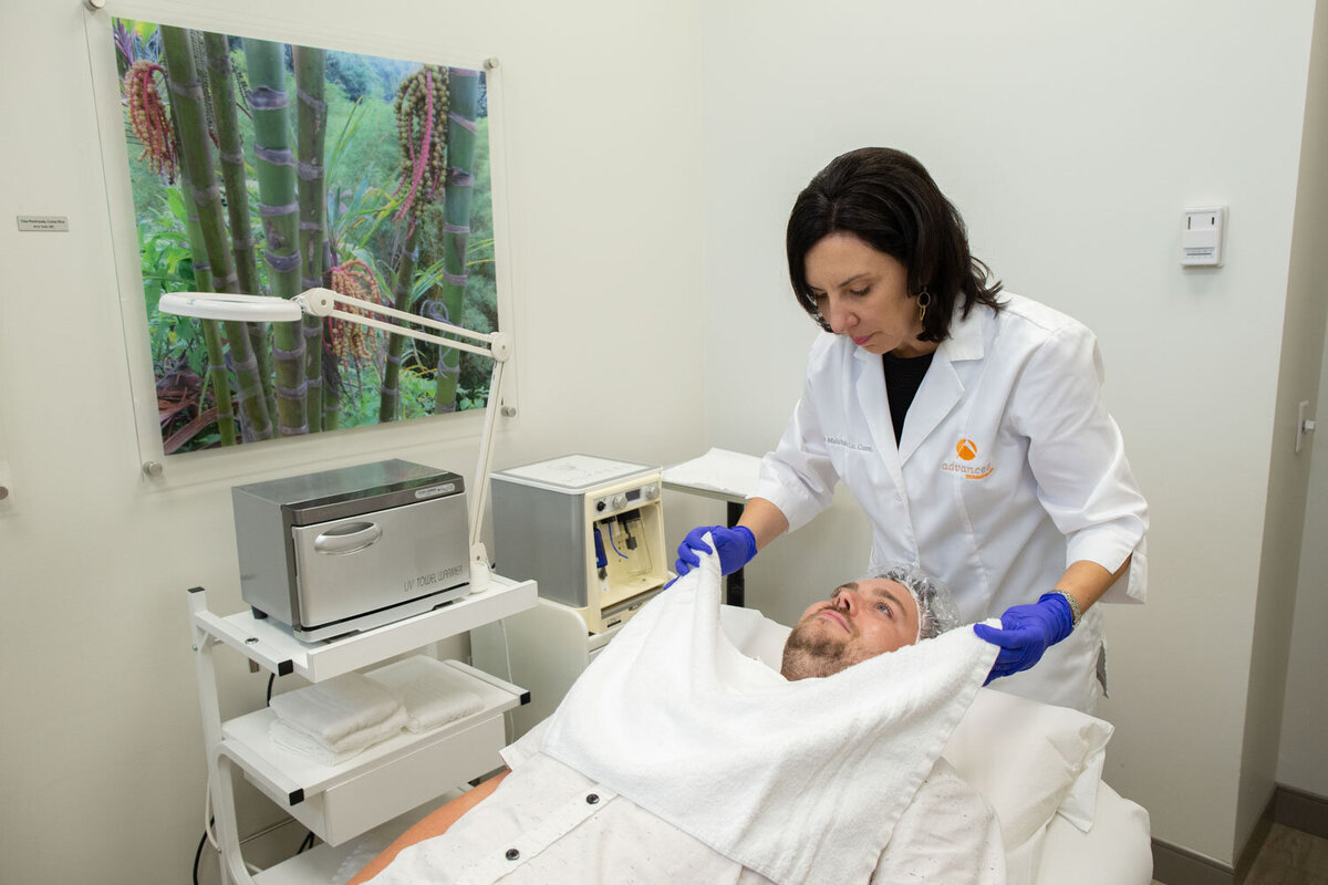 A woman in a lab coat is cleaning a man 's face with a towel