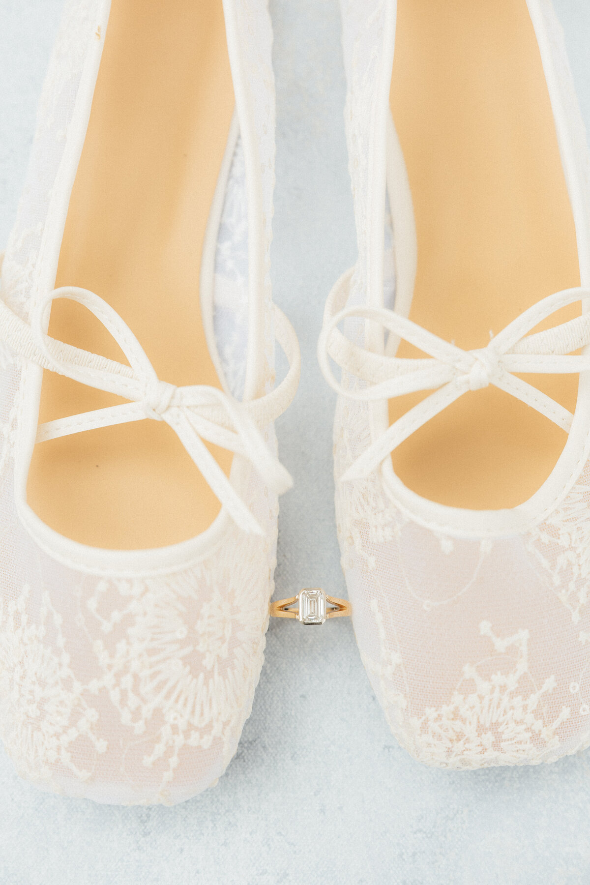 A pair of lace flats with an emerald cut diamond ring balanced between them.