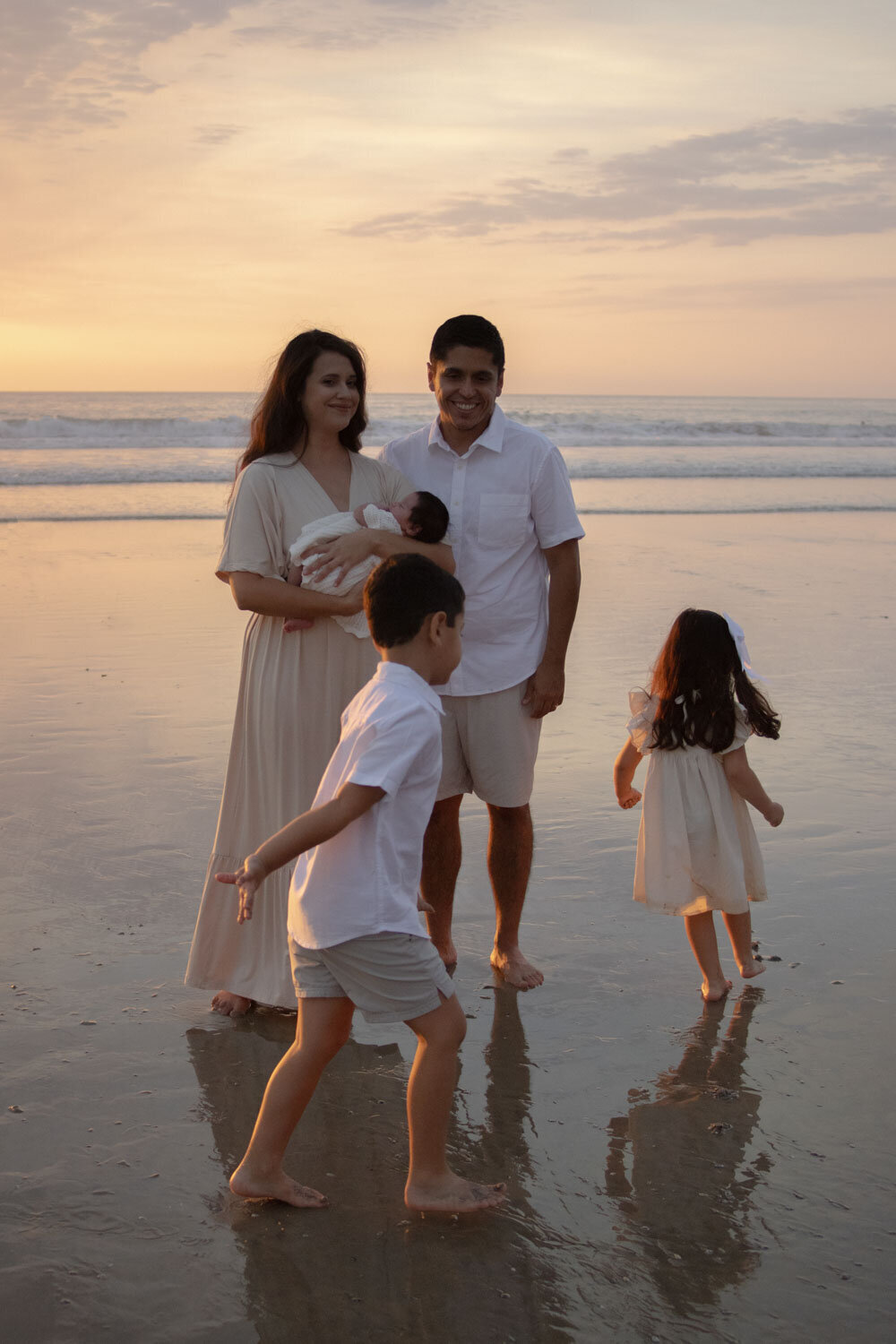 Family standing together on a sandy beach, with the children playing