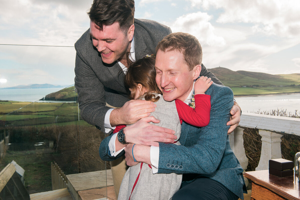 Two grooms hugging small wedding guest