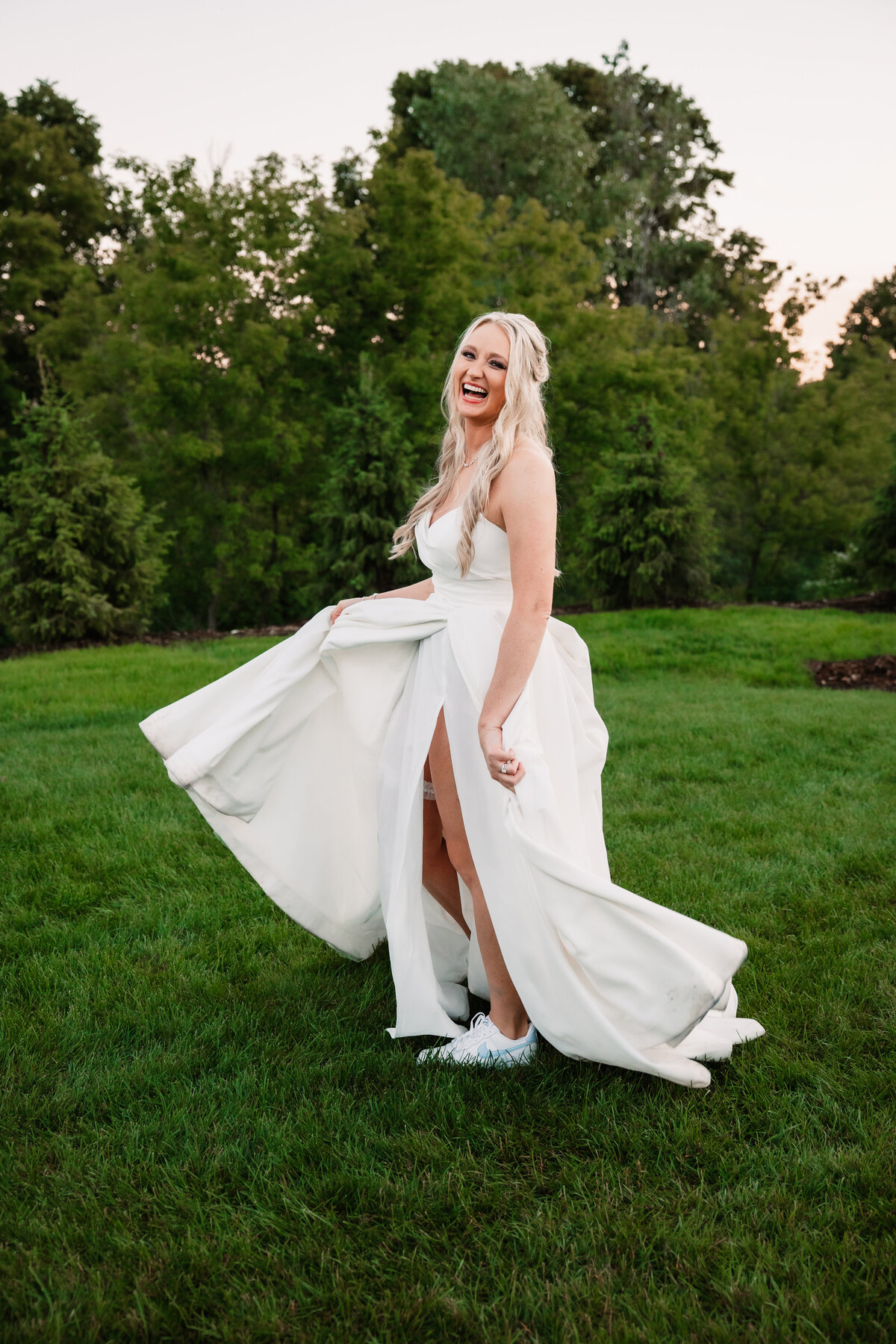 A bride laughs while twirling in a lawn with her dress at sunset