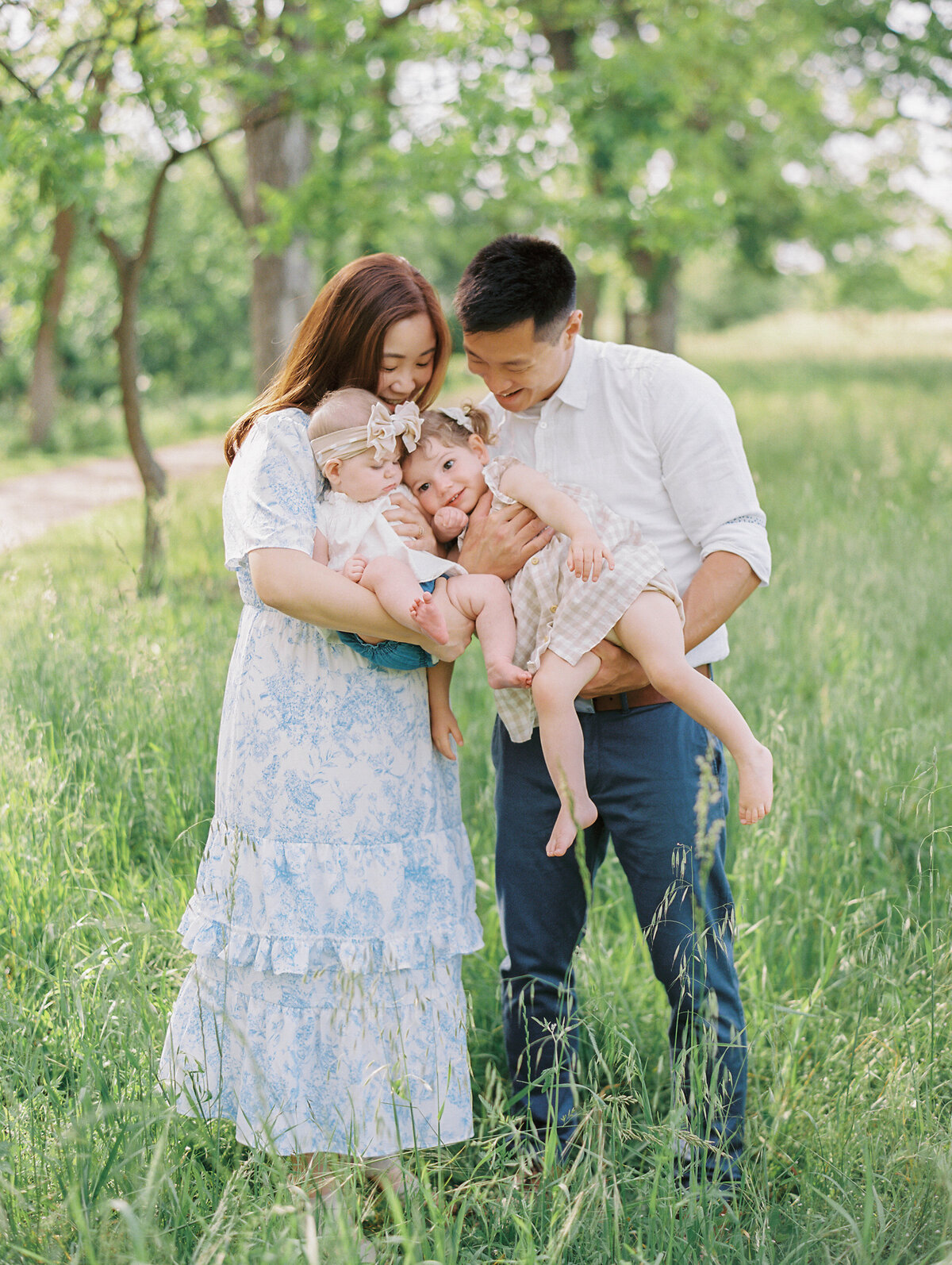 Mom and dad holding their two little girls in a green grassy field