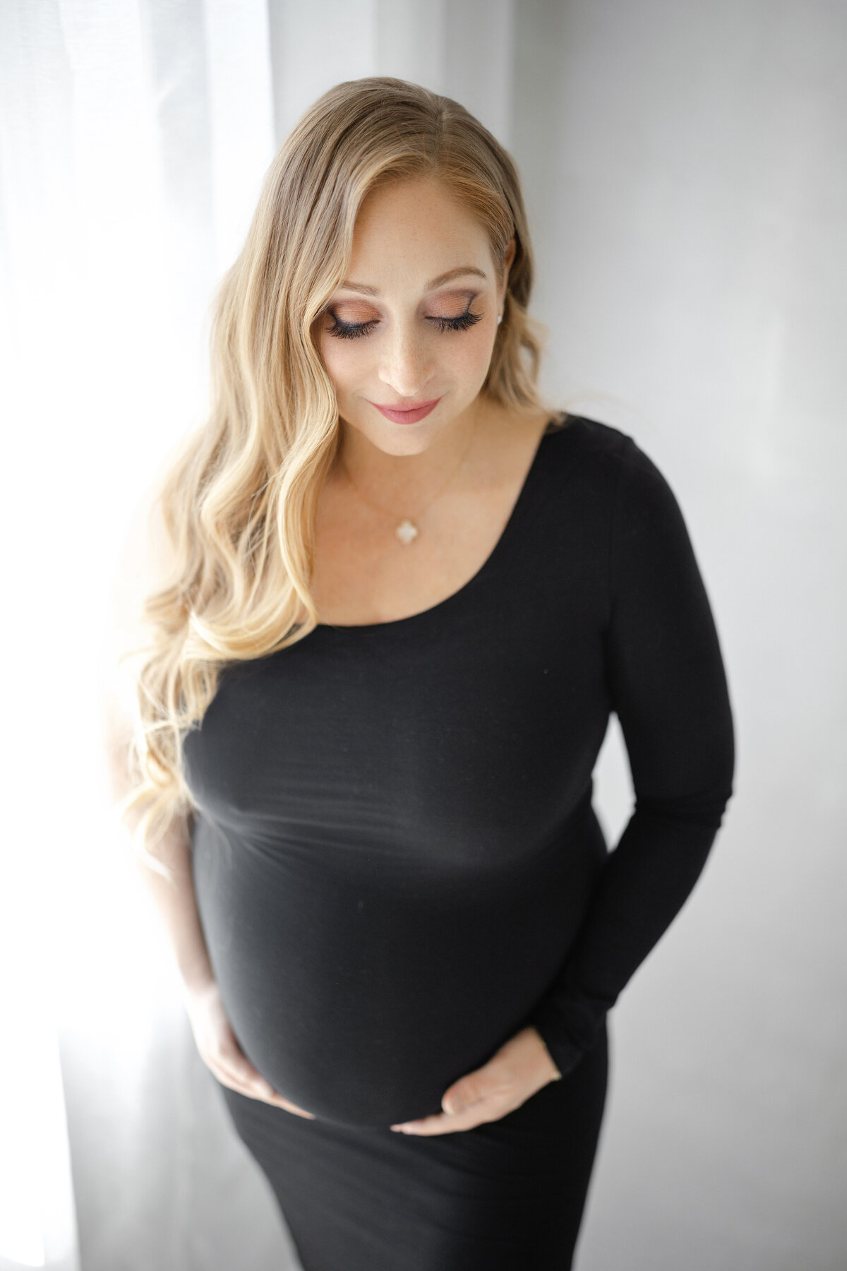 Elegant maternity portrait of Christina standing by window with natural light pouring in during Tampa studio session