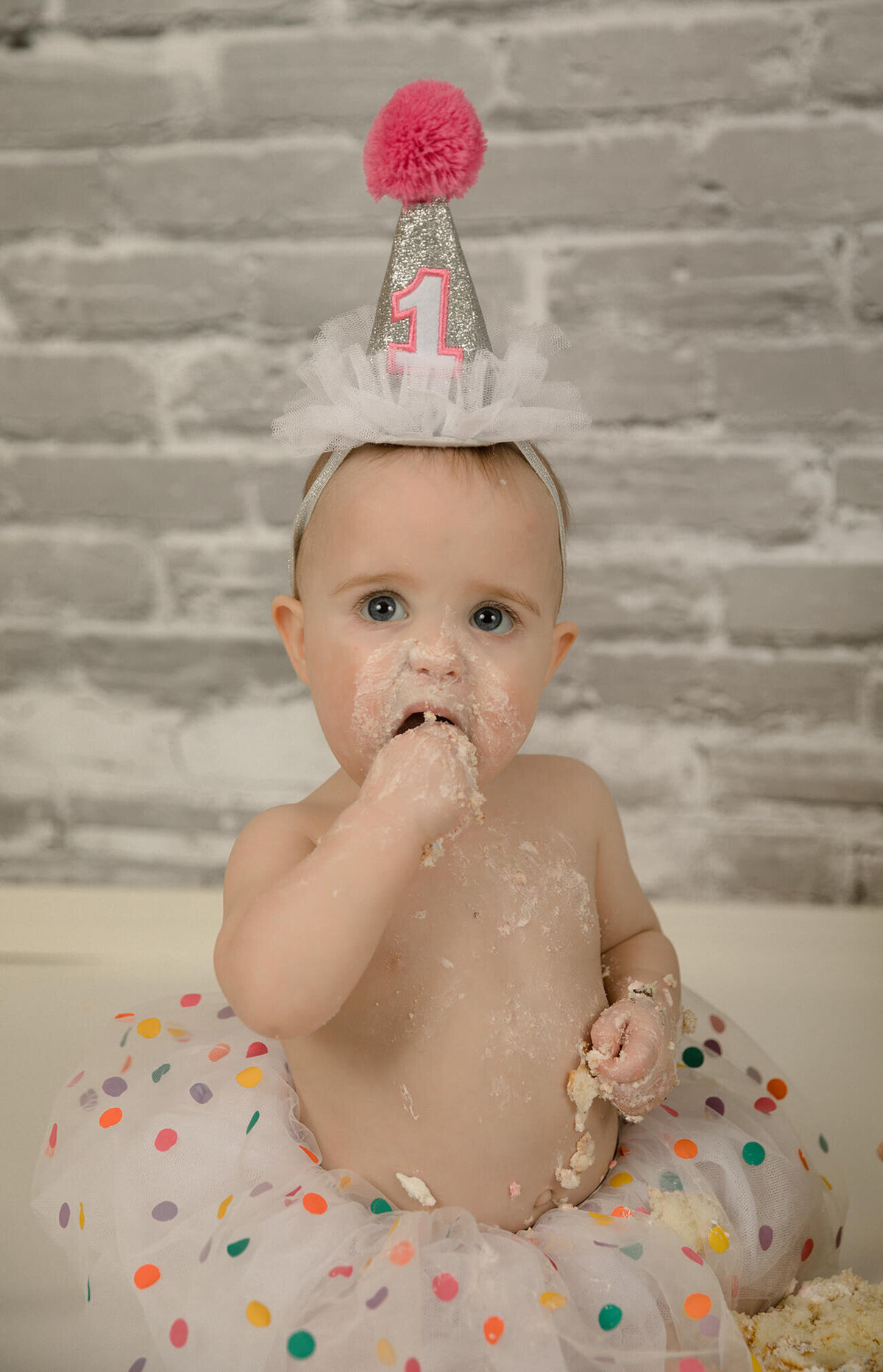 1 year old girl with birthday hat eating cake.