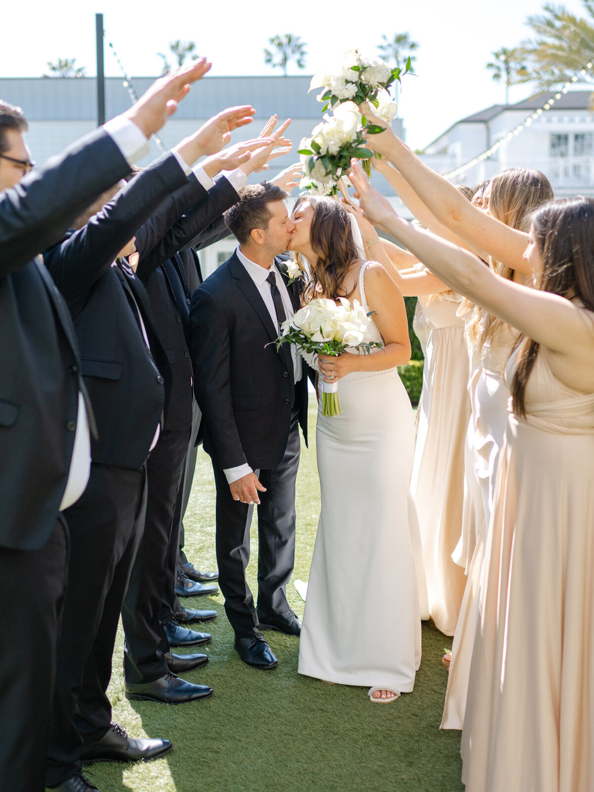 Bride and groom kiss under an arch of raised hands from their wedding party at Lido House