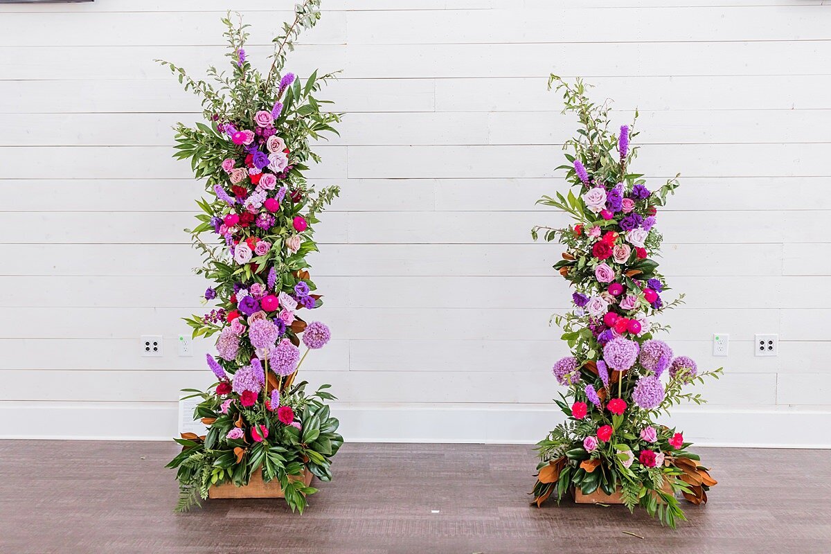 Asymmetrical lush floral arbor with purple, lilac, lavender, hot pink flowers accented with cascading greenery at Sugarfoot wedding.