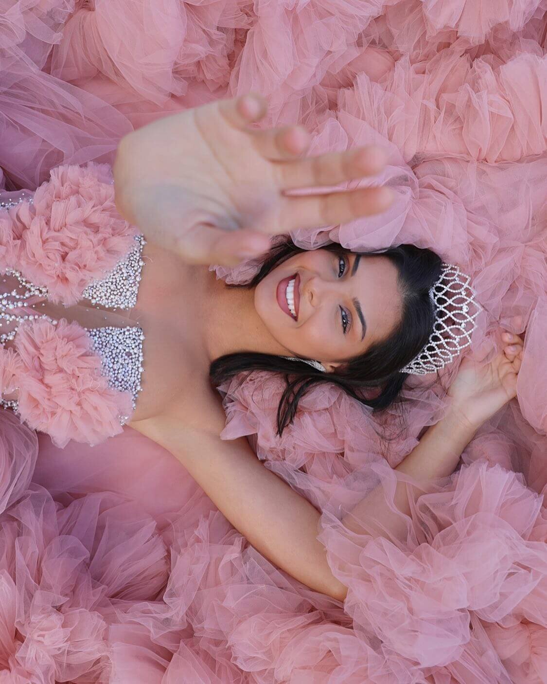 girl laying down on a pink dress and wearing a crown