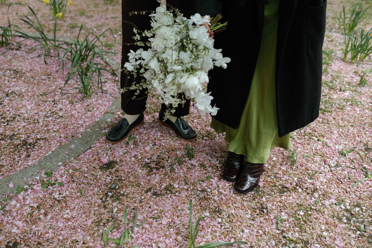 NYC city hall elopement couple with green dress and all white bouquet in the spring with cherry blossom petals