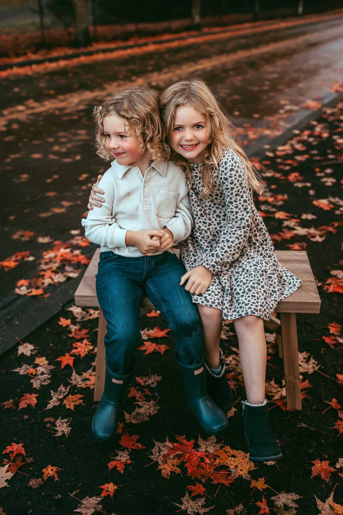 Brother and sister sitting side-by-side on a bench in Renton, WA, smiling sweetly at the camera during a fall family session.