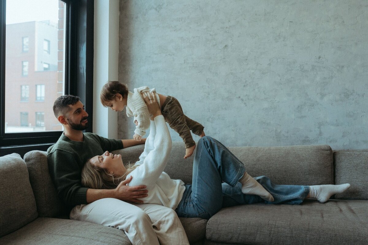 couple lying on couch holding son above them during in home family photos captured by NYC family photographer Elsie Goodman