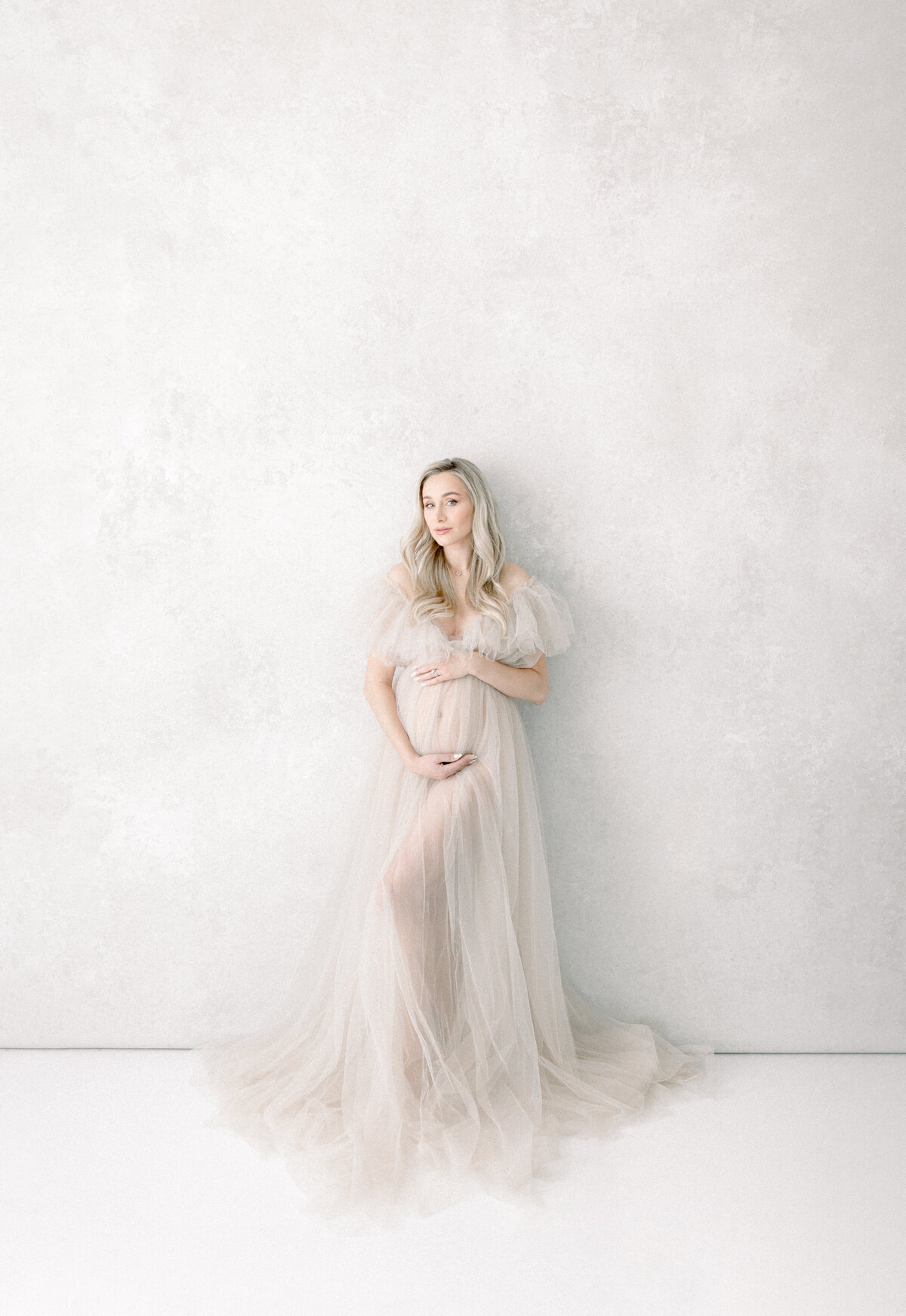 Expecting mother in a tulle gown holding her belly