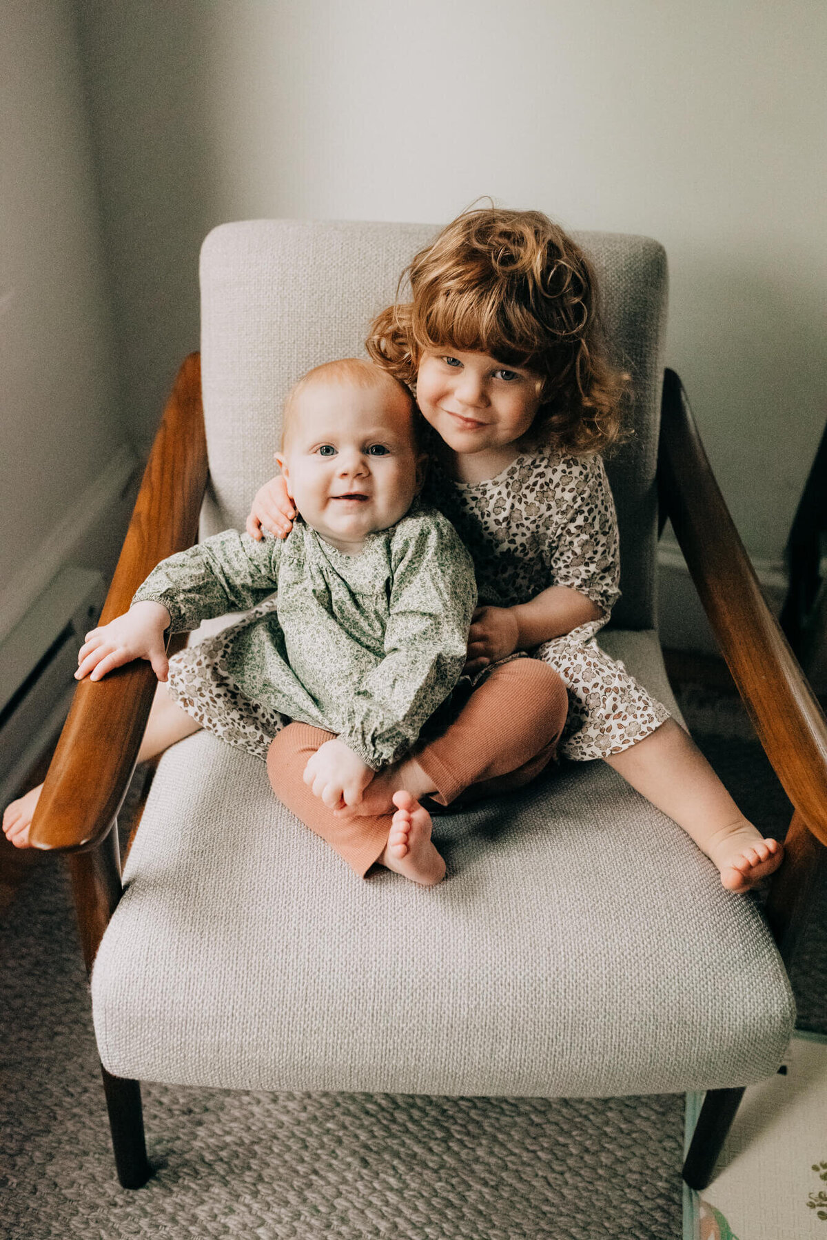Two young girls with red hair sit together on a chair in the big sister's room