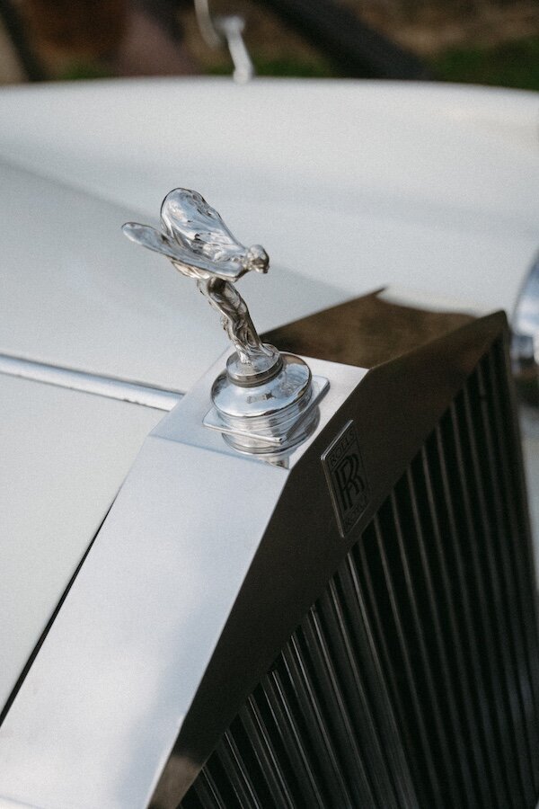 Emblème Rolls-Royce scintillant sur le capot d'une voiture d'exception. Photo Kamescop, reportage mariage au style vintage.