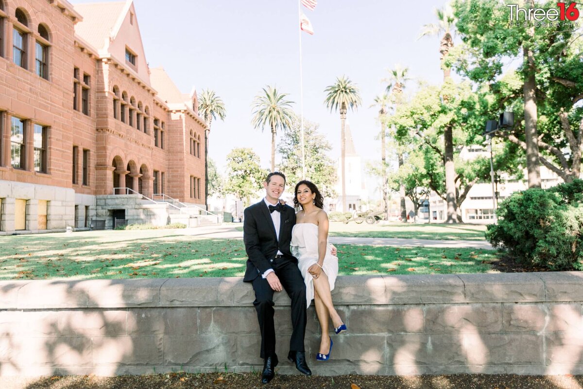 Bride and Groom sit on a wall together outside the courthouse after their elopement services were over