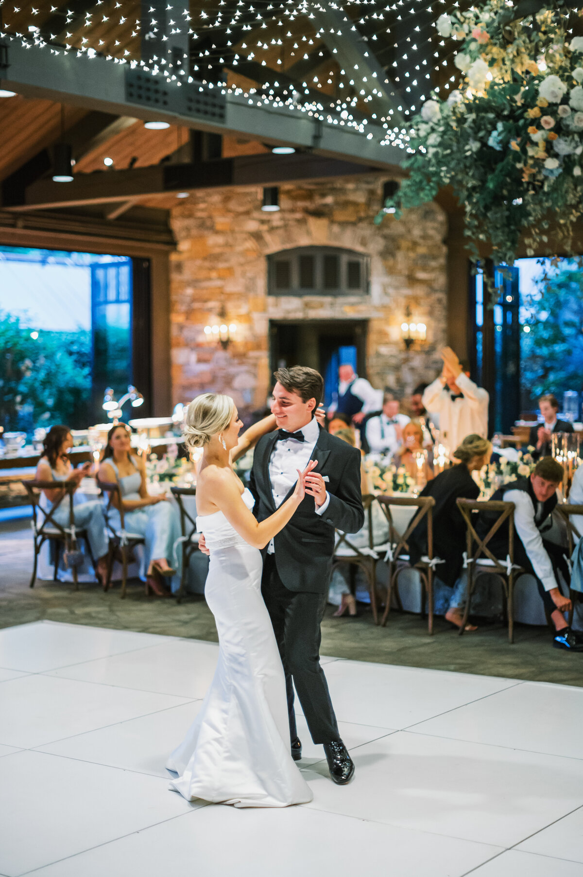 Bride and groom share their first dance under twinkle lights and floral installations at Old Edwards Inn wedding reception in Highlands, North Carolina.