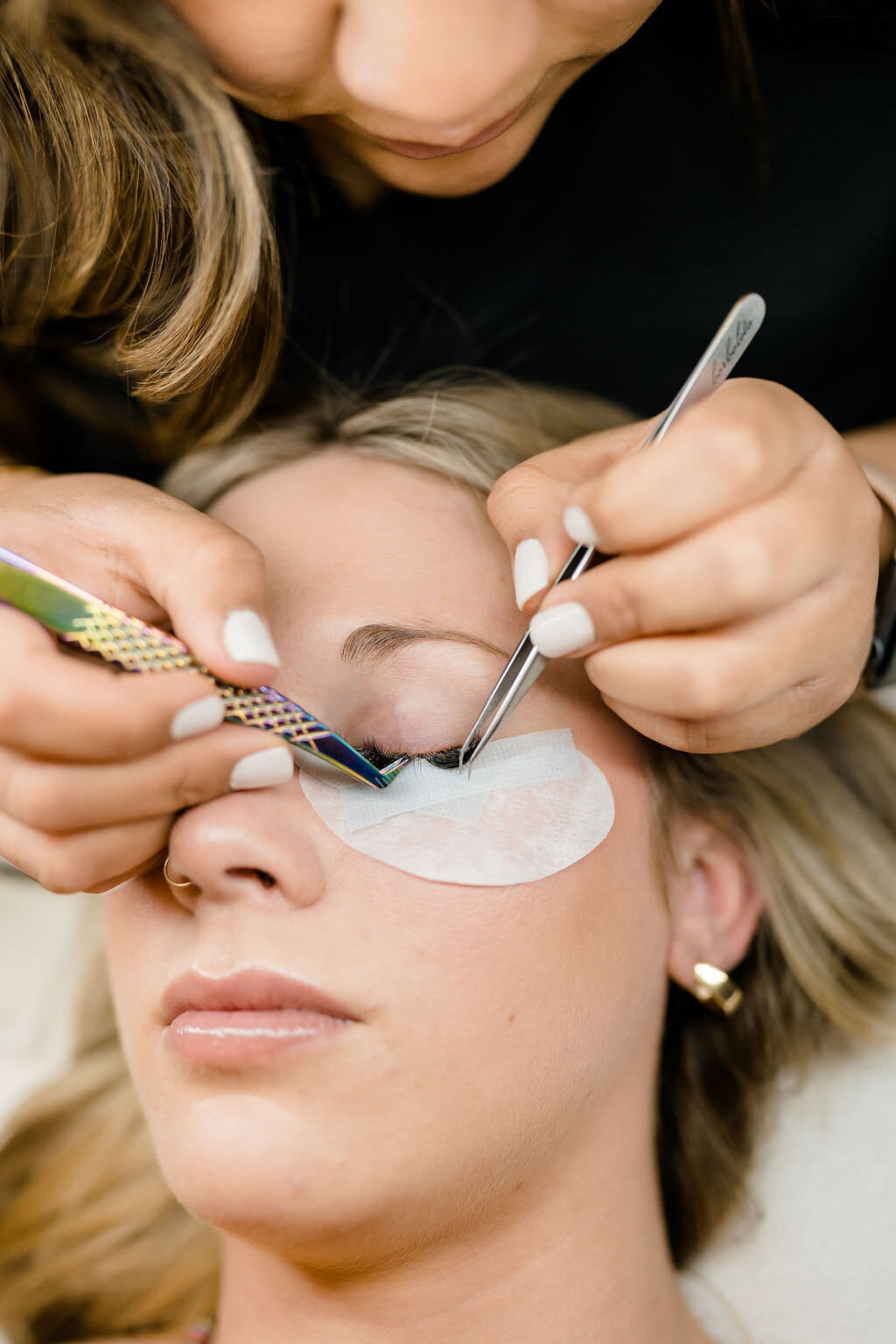 woman holding two pairs of tweezers as she put eyelashes on another woman