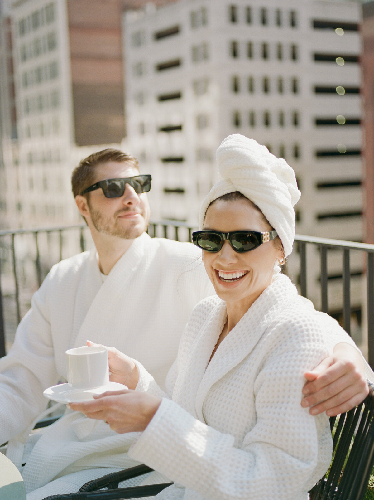 smiling couple in bathrobes share coffee, brunch on Shinola Hotel balcony
