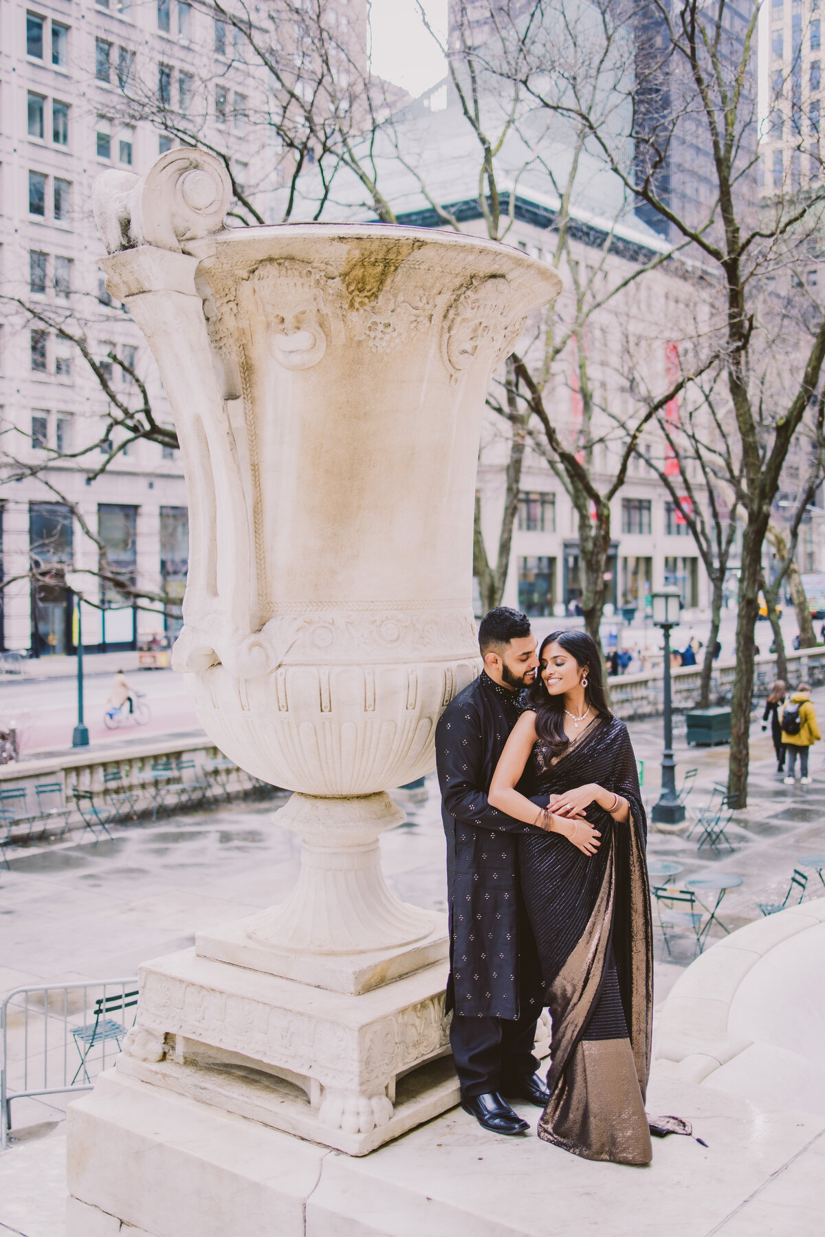 A couple standing outside in indian sari clothing by a statue at the new york public library in nyc during their engagement shoot