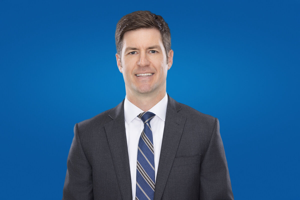 Cincinnati headshots showcase: A professional male in a sharp gray suit with a complementing striped tie stands out against a vibrant blue background. His confident expression and poised demeanor reflect the ideal corporate portrait, capturing both sophistication and approachability