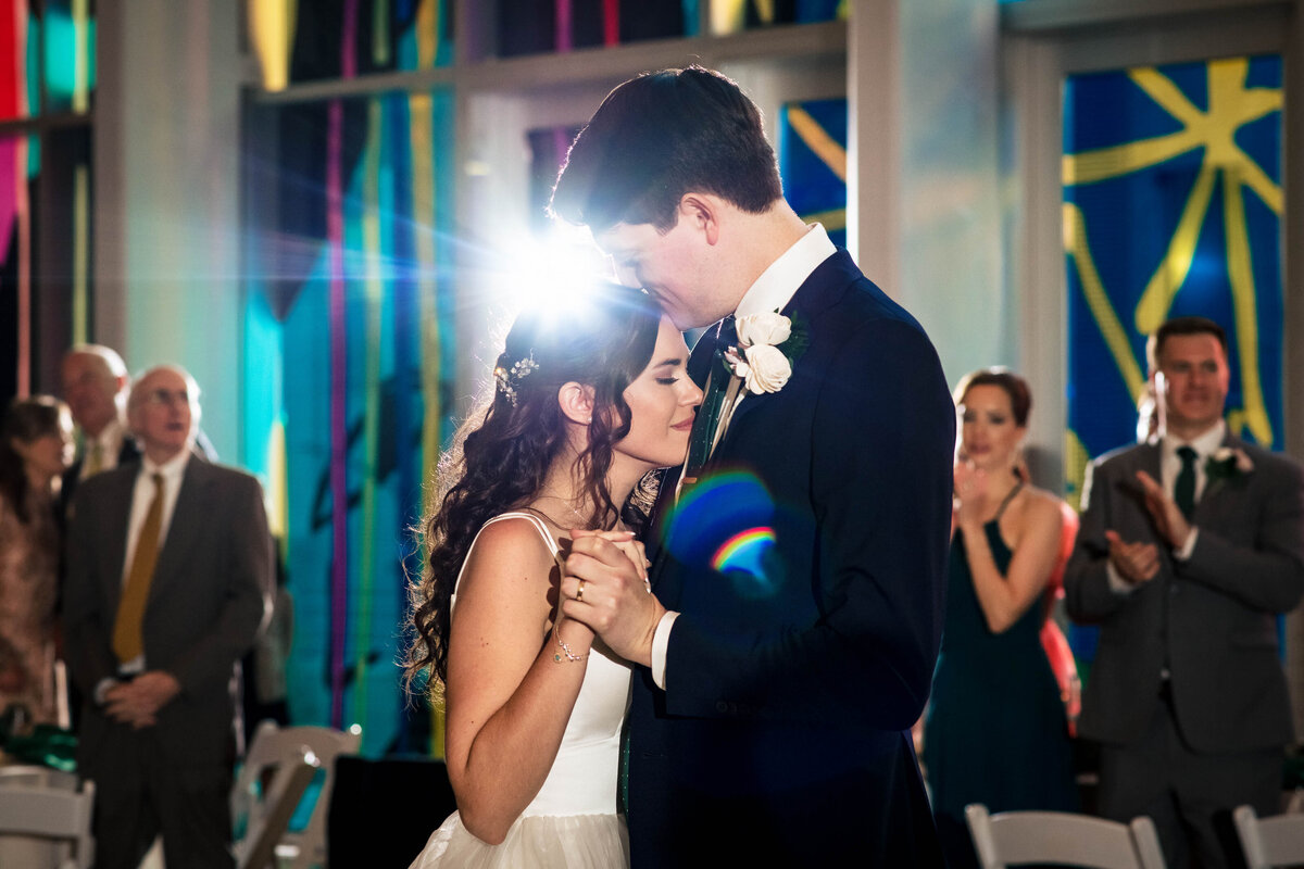 Groom-kissing-bride's-head-cuddled-close-during-their-first-dance-at-the-Mint-Museum-Uptown-in-Charlotte