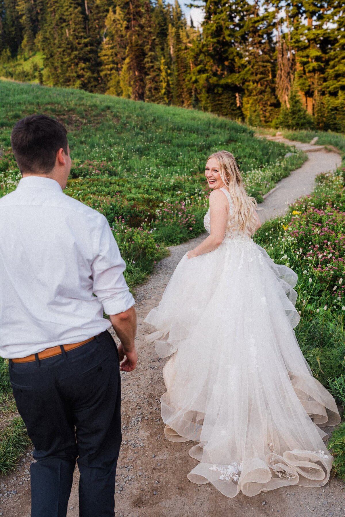 bride looking over her shoulder at groom chasing her on mount rainier hiking trail.