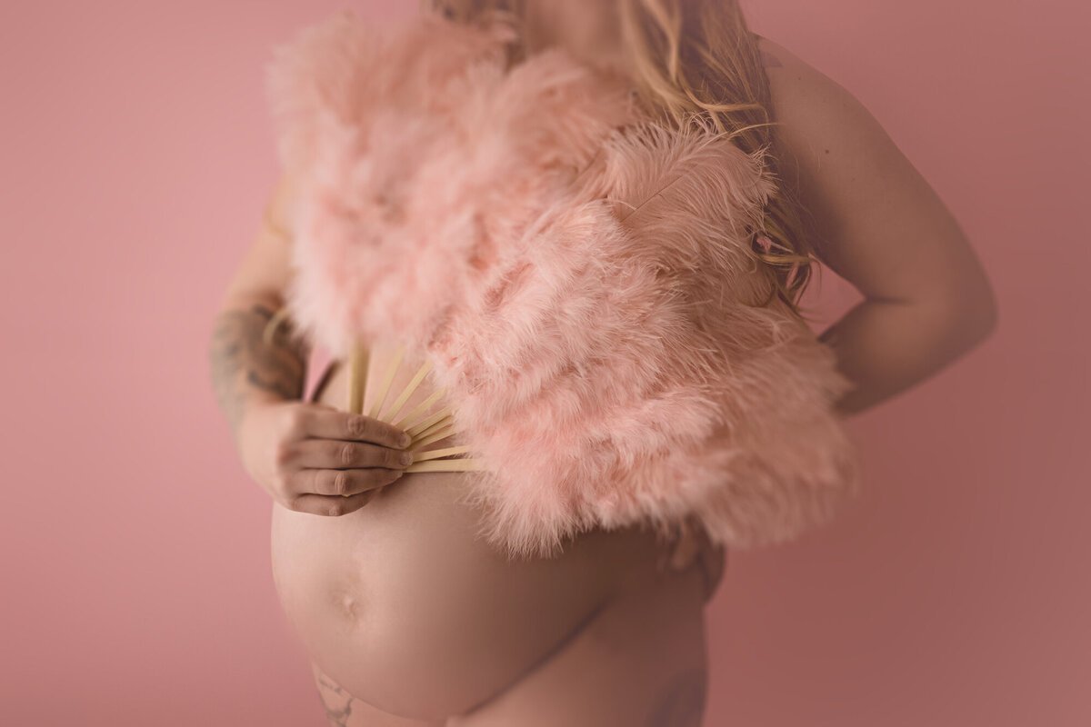 Details of a mom to be's bump while covering her chest with pink feather fan