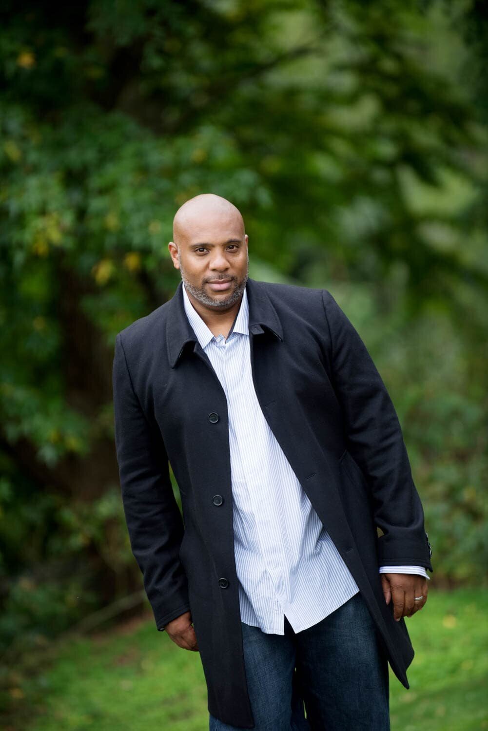 Professional portrait of gentleman in black trench coat outside at the park.