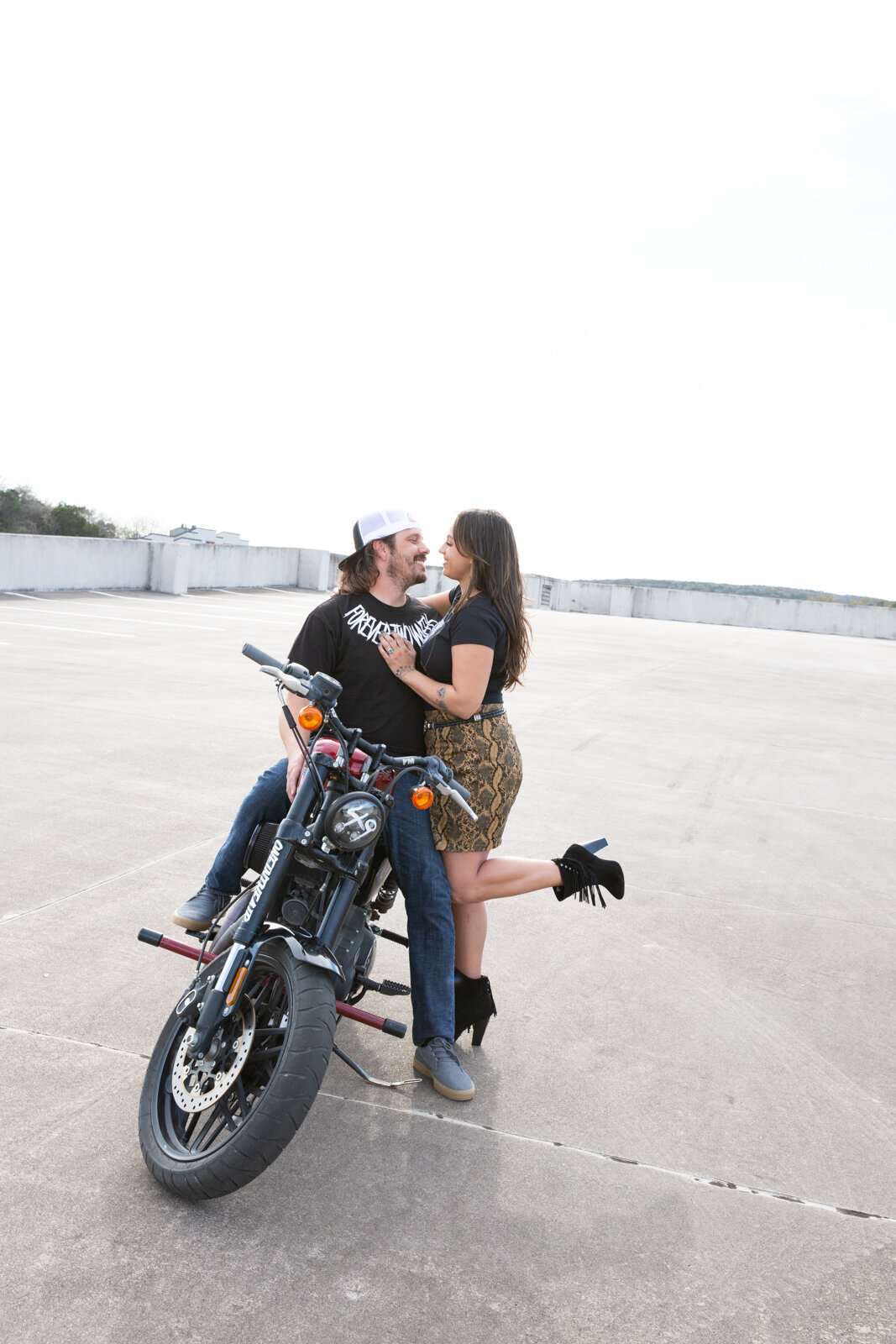 A couple kissing on a motorcycle in a parking lot captured beautifully by an Austin wedding photographer.