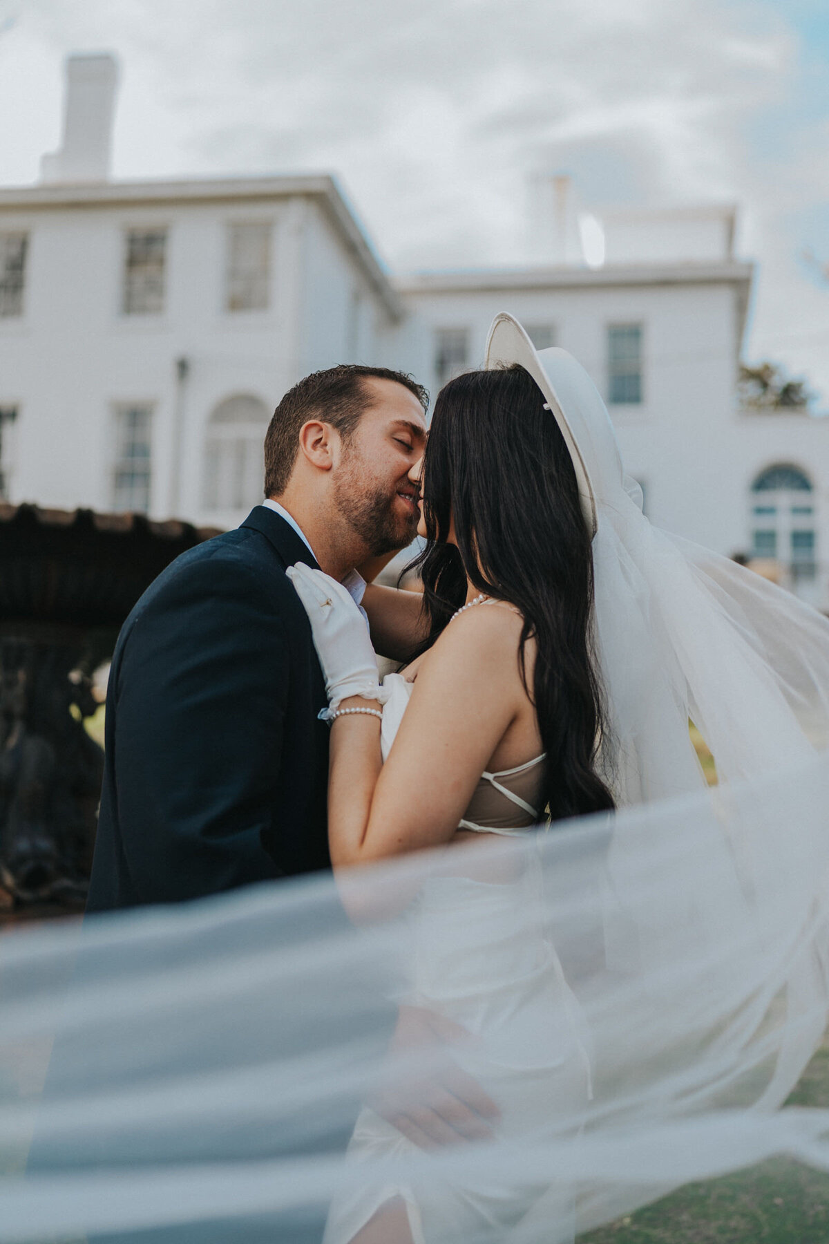 Woman's veil blows in the wind while she kisses her husband