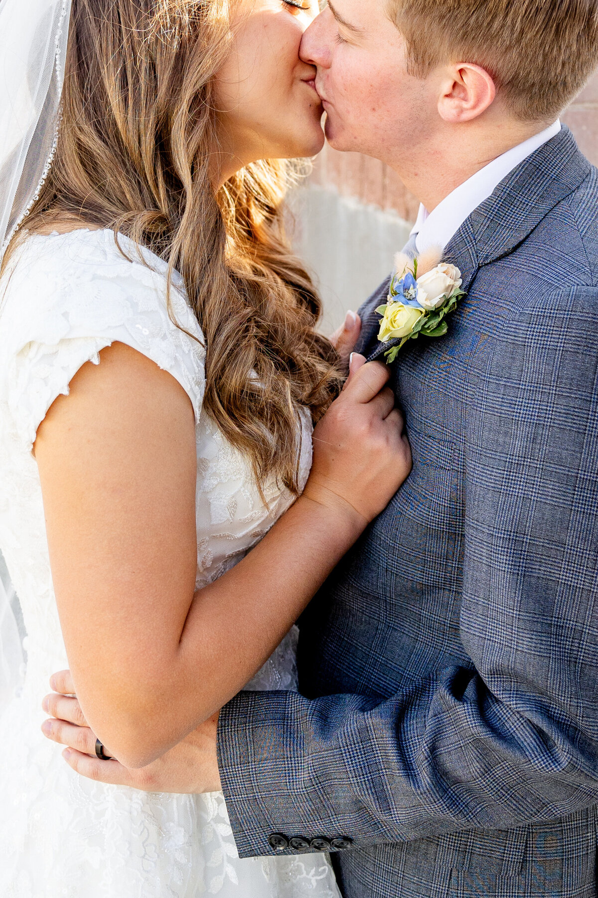 A close-up shot of a newlywed couple sharing a gentle kiss, highlighting the bride’s delicate lace dress and the groom’s elegant boutonniere.