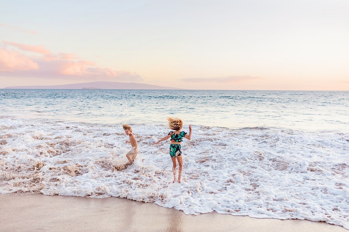 Two kids in swimwear jump over oncoming waves in Wailea while on their Maui vacation