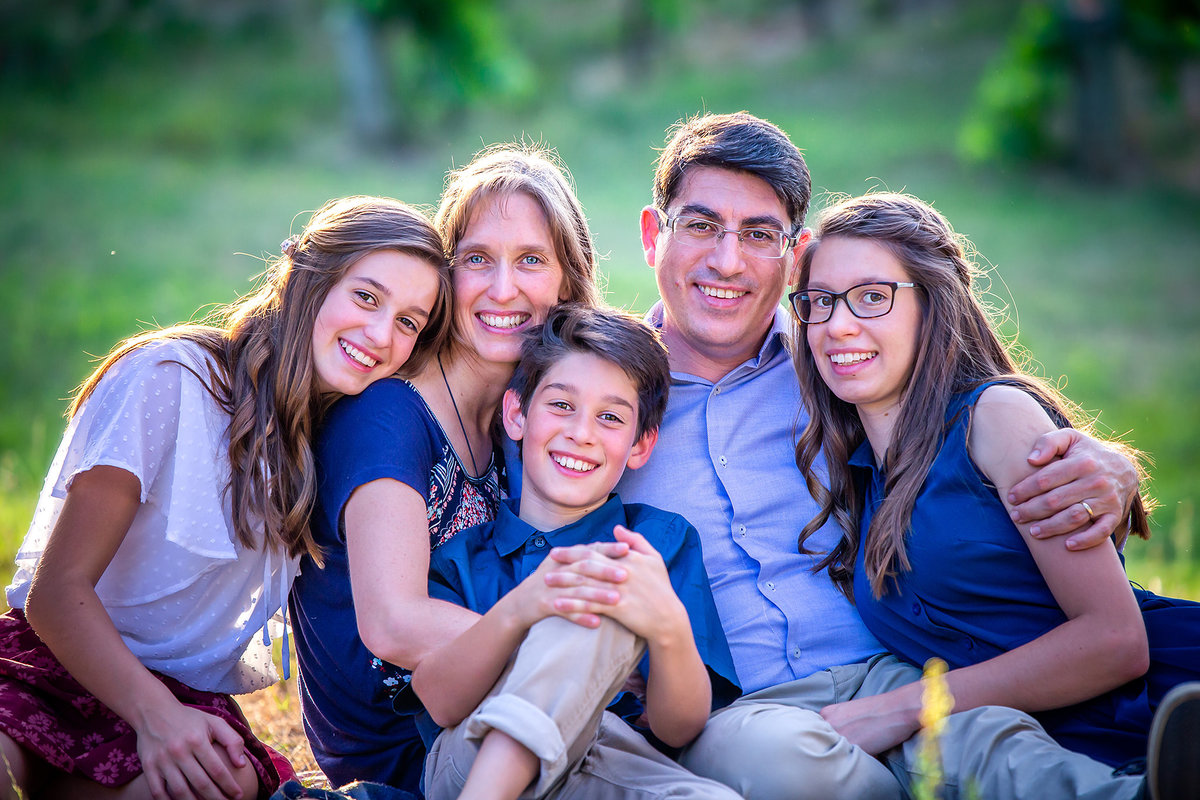 Outdoor family pictures with teenagers as the mother and father sit together in the grass and their teenagers cuddle up next to them