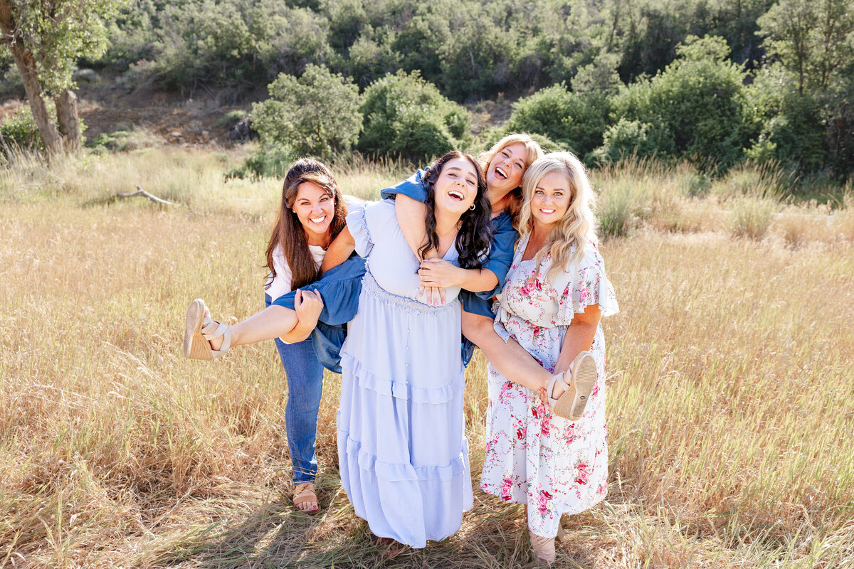 Four sisters having fun in a beautiful open field, sharing laughter and playful moments during a family photoshoot.