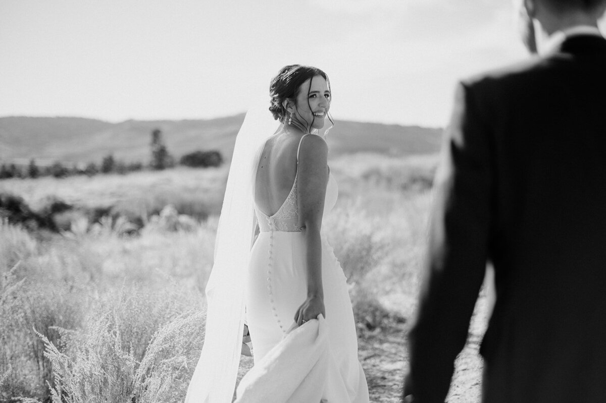 Modern bride leads her groom down a grassy field while looking at him lovingly.