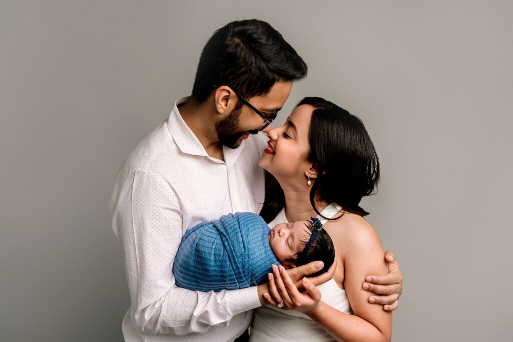Professional Connecticut newborn photographer creates intimate family moment with parents gazing lovingly at their newborn baby in studio setting