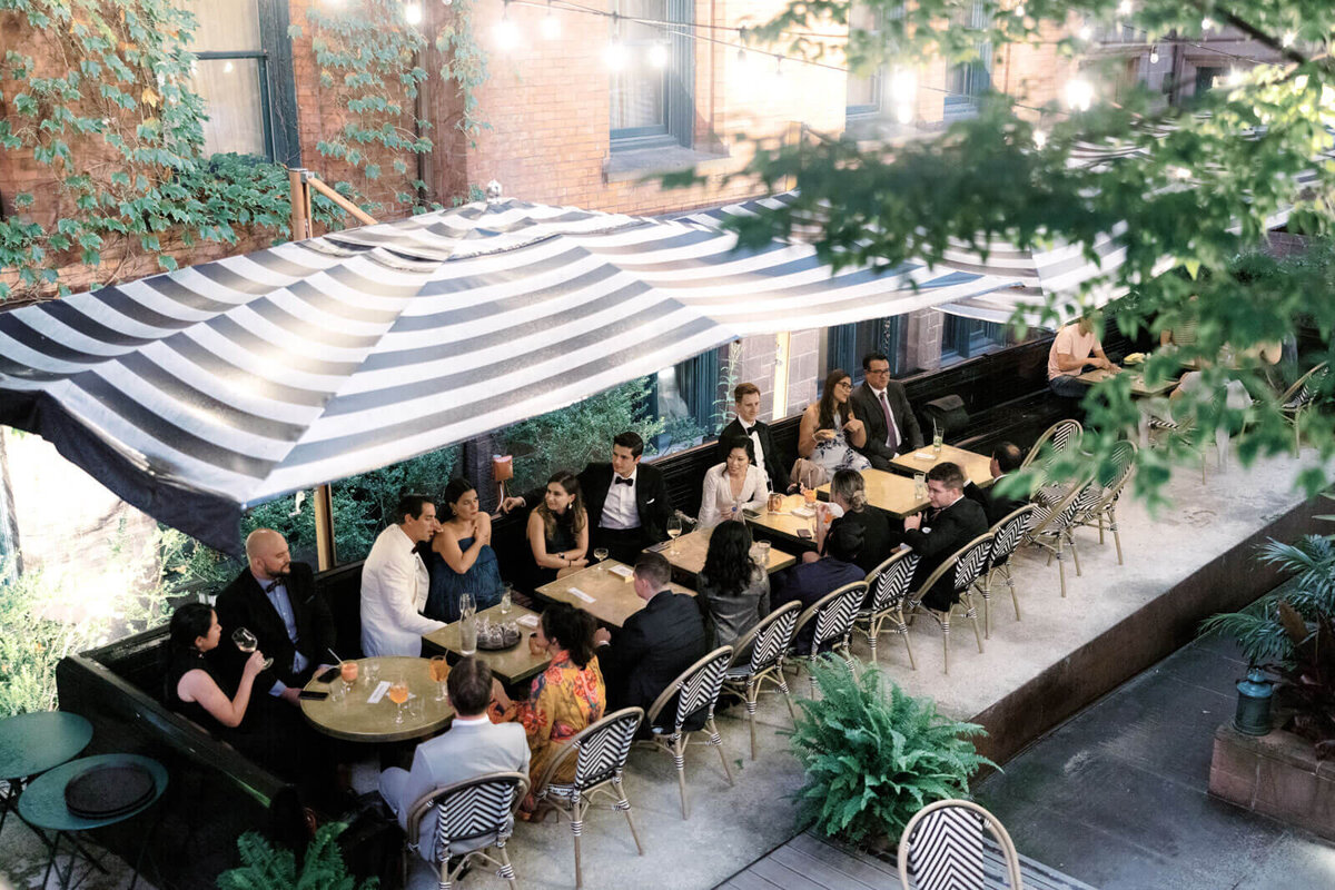 Top view of the bride, groom, and guests chatting at an outdoor dining area at The High Line Hotel Chelsea, NYC. Image by Jenny Fu Studio
