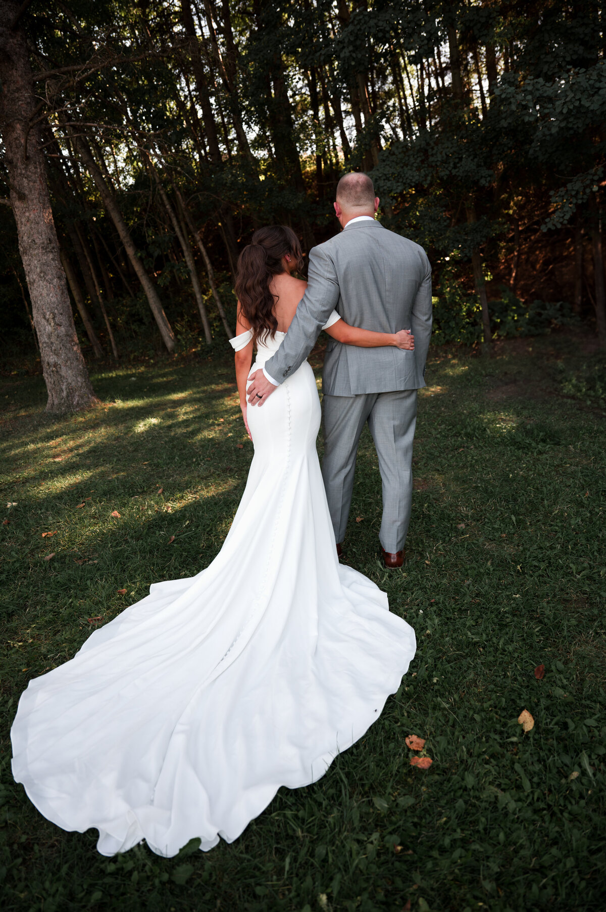bride and groom standing facing the forest with backs to camera