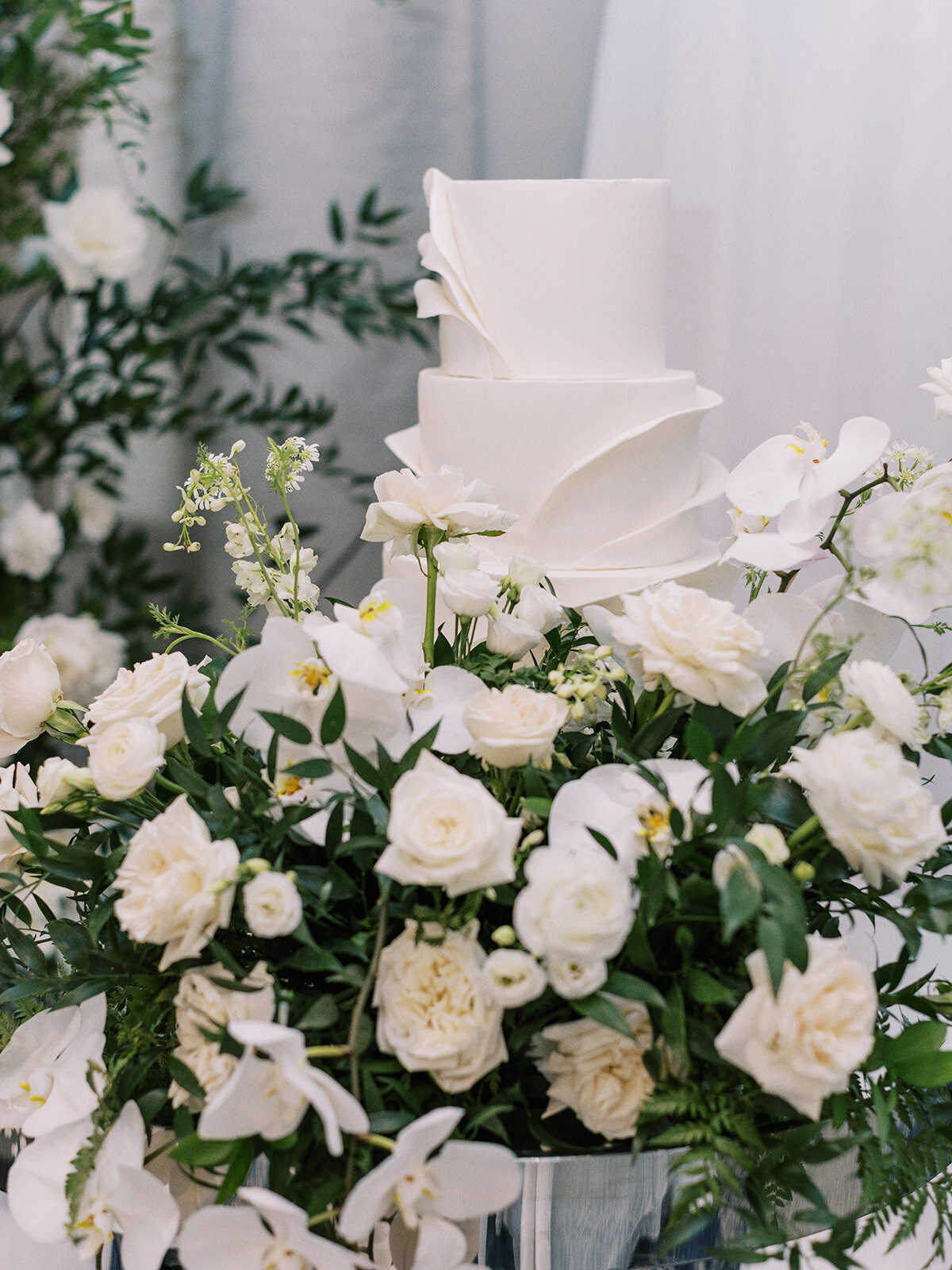 A three-tier white cake with smooth fondant is decorated with white flowers and greenery at its base, perfect for a classic Calgary wedding.