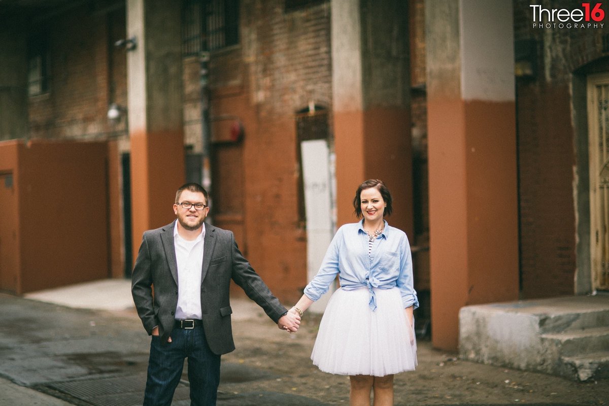 Engaged couple hold hands while walking in the Santa Ana Historic District