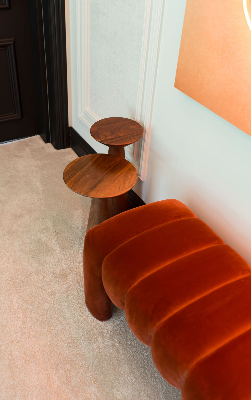 A cushioned, burnt orange velvet bench flanked by two wooden side tables.