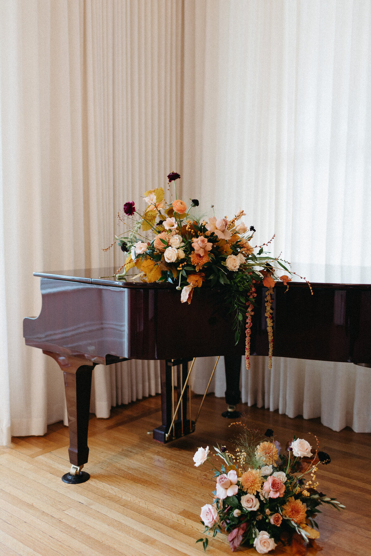 A grand piano, adorned with pink and orange flowers, sits elegantly on a wooden floor. Curtains drape in the background, while more blooms scatter gracefully around. This scene captures a timeless moment that any Toronto wedding photographer would cherish.