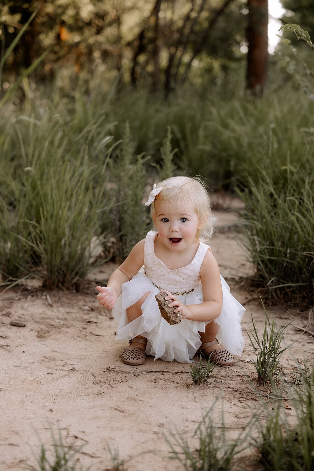little girl playing with the rocks she found. She is looking at the camera.