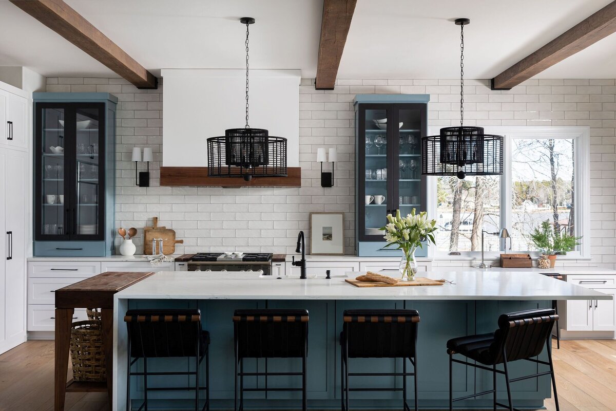 kitchen with white and blue accent cabinets, waterfall edge island, and black pendant lights