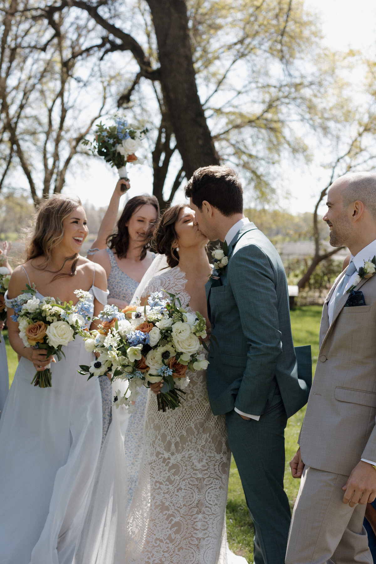 Bride and groom kiss joyfully as the wedding party cheers, celebrating their love on a beautiful day.