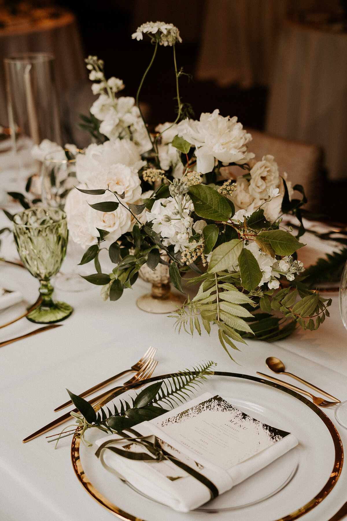 Elegant centerpieces of white roses and greenery decorate a Restaurant Beatrice wedding reception.