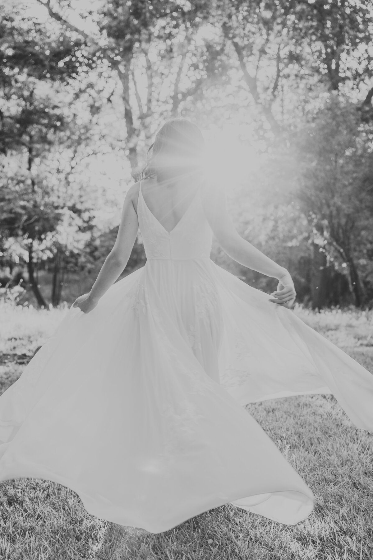 Black and white of bride spinning her dress around with sun shining.