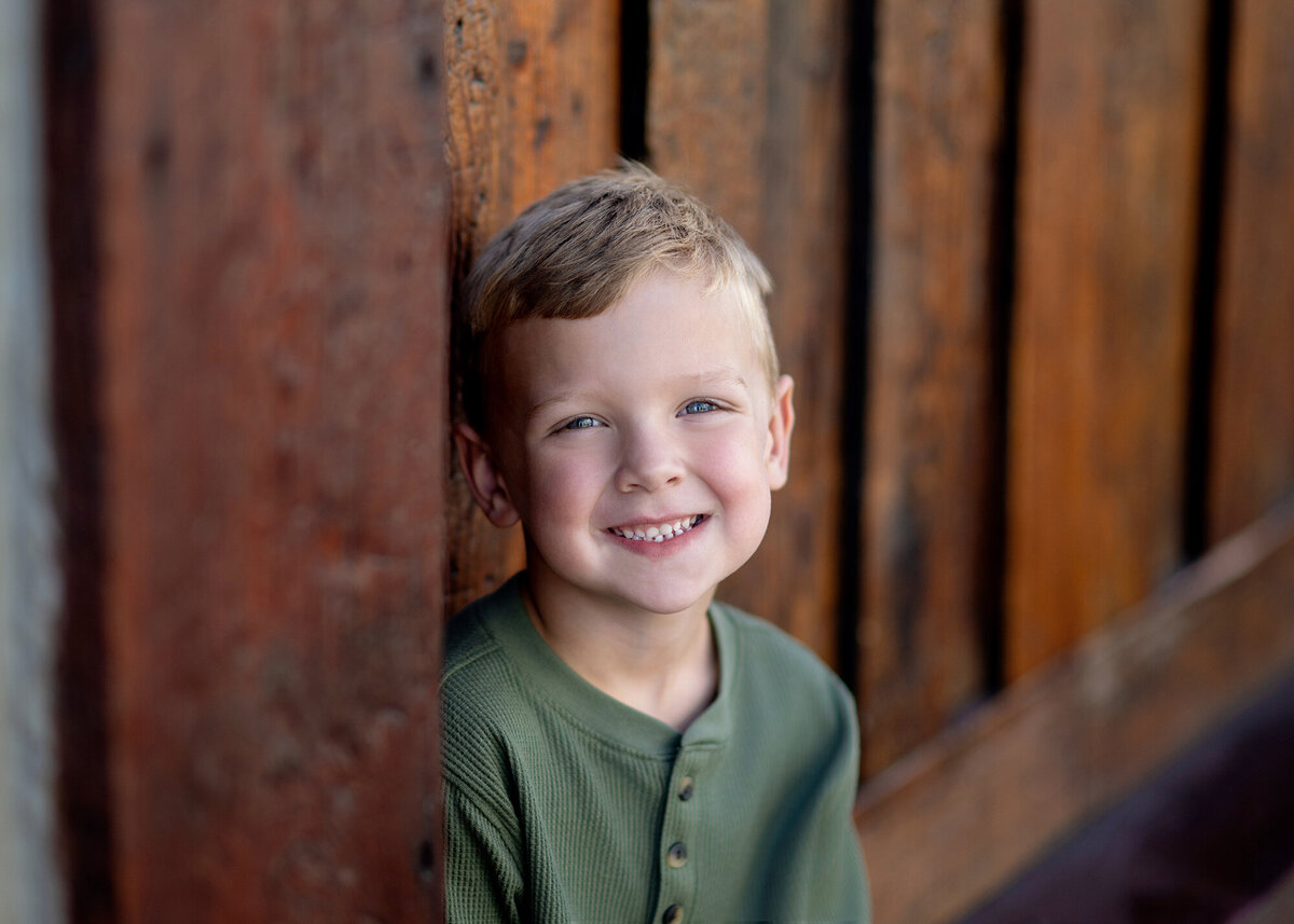 A child stands alone against a painted wooden wall, their smile bright