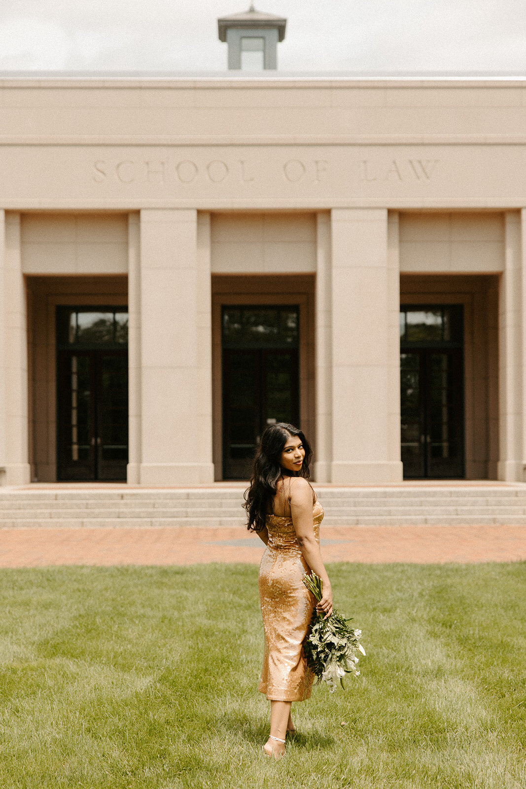 Graduate posing with flowers in front of UVA Law building